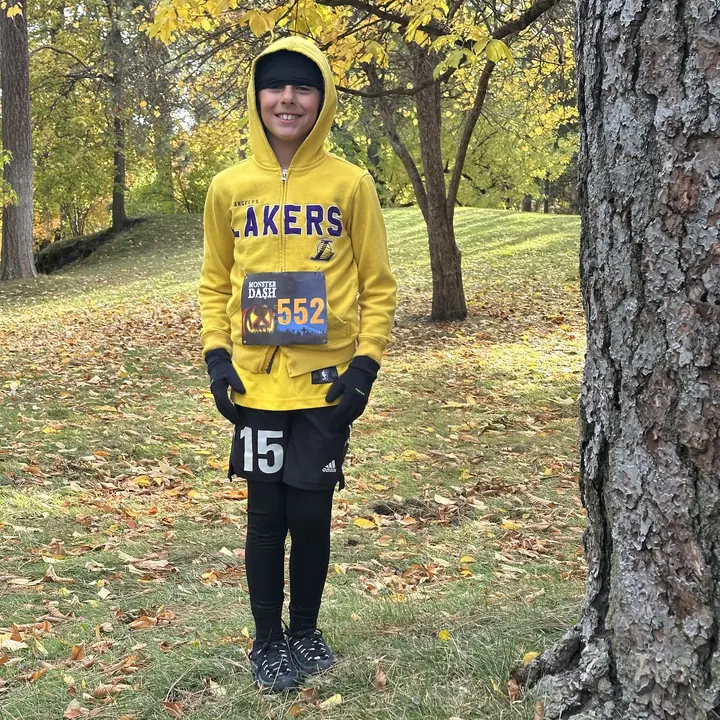 Boy in a yellow hoodie wearing a Monster Dash race bib in a park