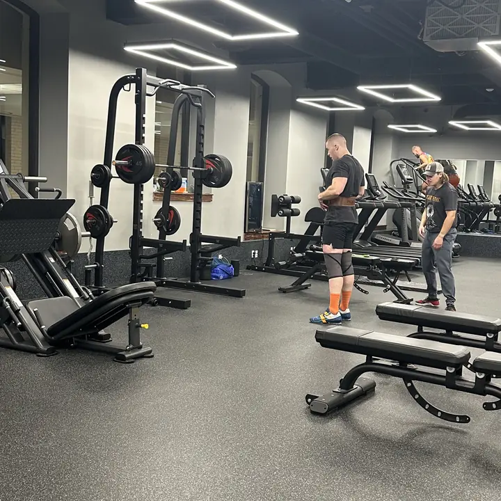 The gym floor with racks and benches, a lifter putting on his belt