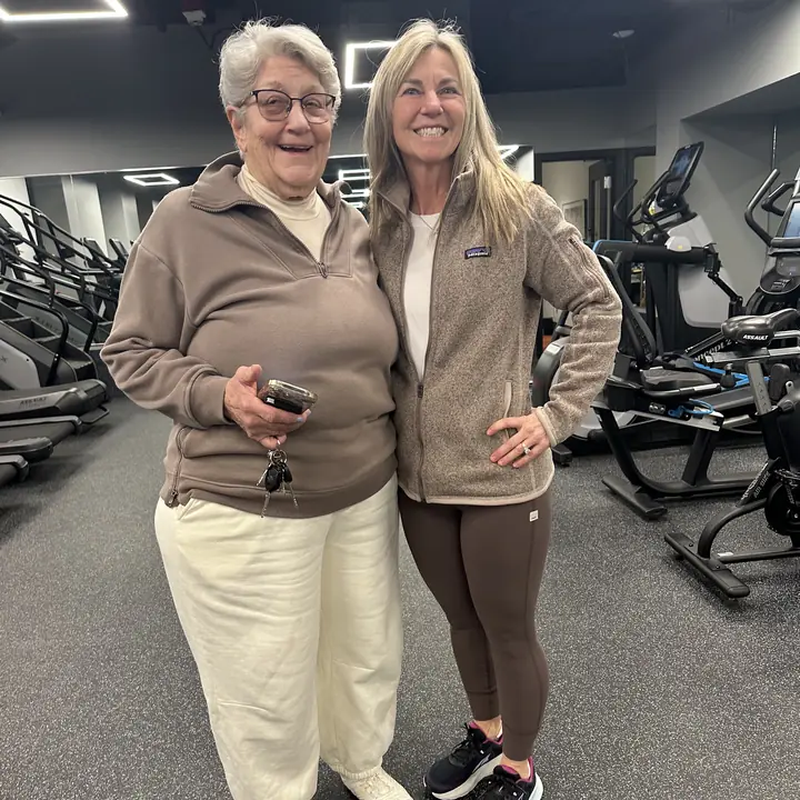Two women smiling arm in arm beside the cardio machines
